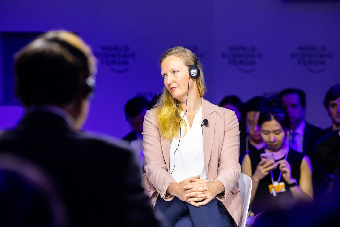 A blonde woman wearing a head set sits with her legged crossed during an event at the World Economic Forum 