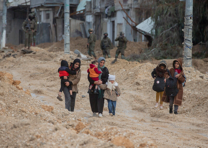 A group of women and children walk along a muddy path in Nur Shams refugee camp.