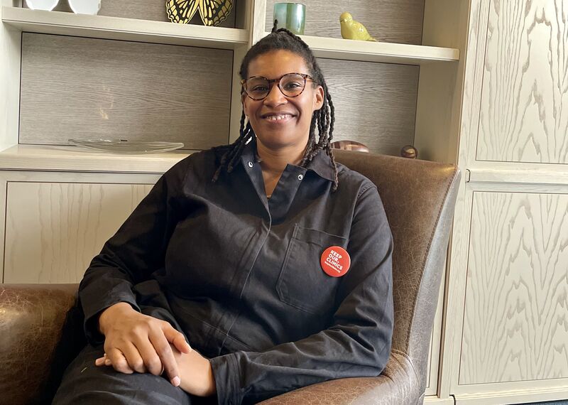 Erin Grant, a Black woman with braided hair and glasses, is looking at the camera smiling as she is sitting with her hands on her lap. She is the co-Executive Director of Abortion Care Network.