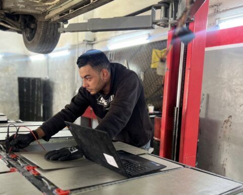 Man leans over large depleted EV battery in a workshop in Amman