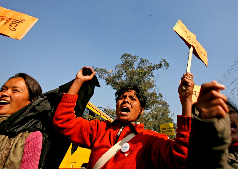 A group of women stand against the bright blue sky, holding yellow placards in the air