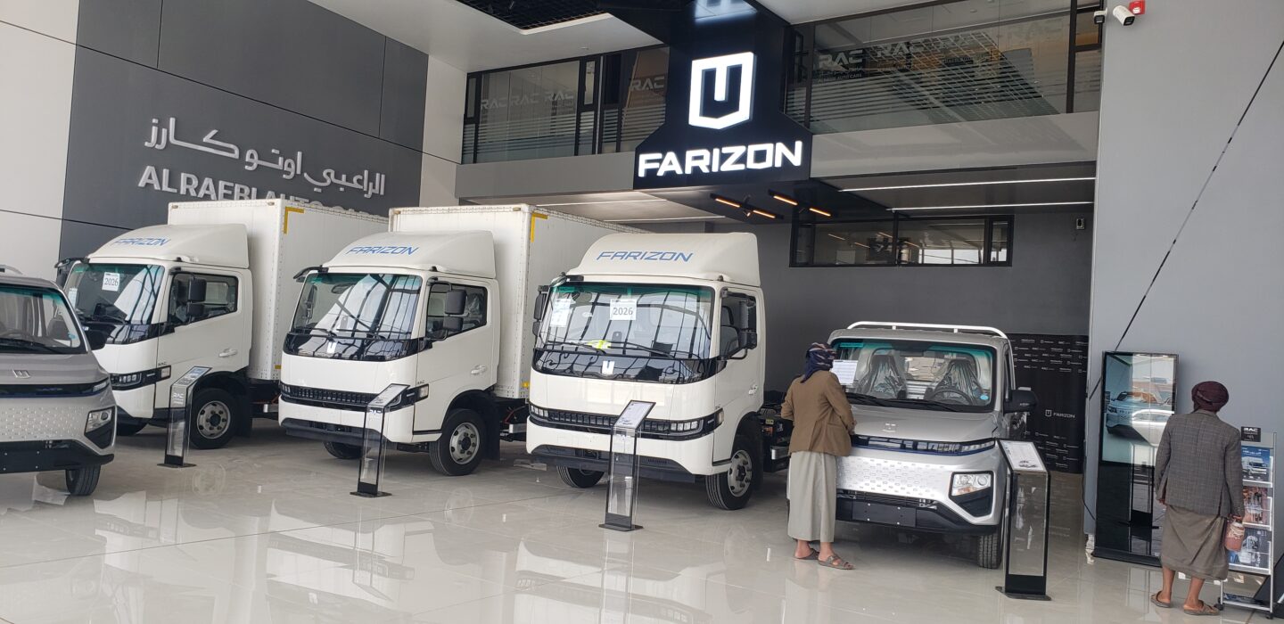 People look at four large Chinese electric trucks in a show room in Sanaa, Yemen
