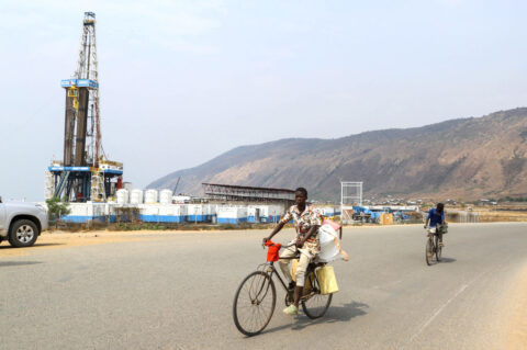 Residents cycle past an oil drilling rig of the Kingfisher oilfield on the shores of Lake Albert operated by China National Offshore Oil Corporation (CNOOC)