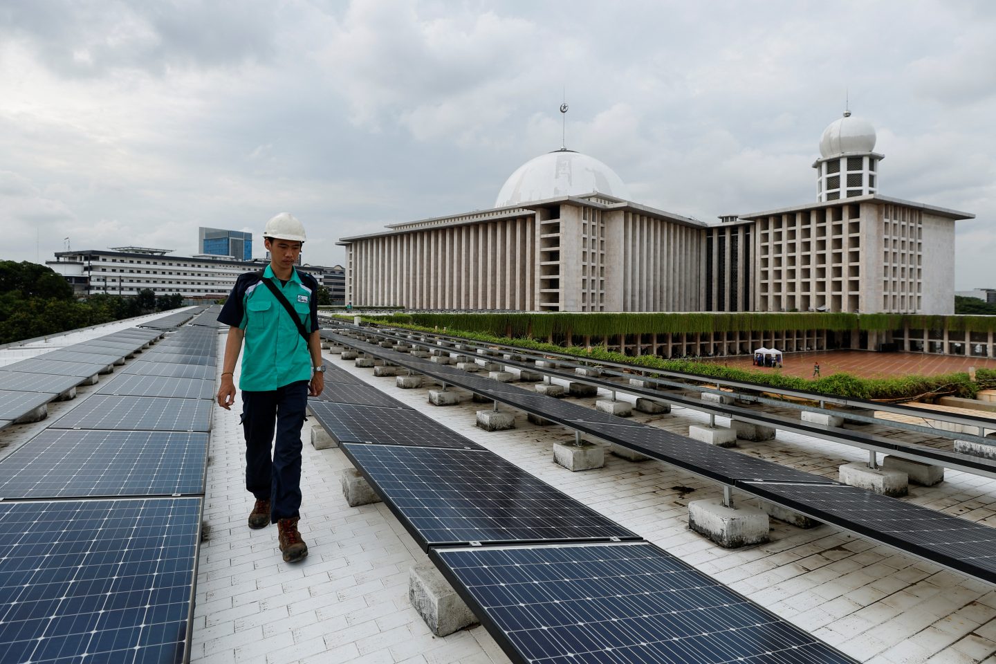 A technician in a green shirt walks next to solar panels that partially provide electrical power to the Grand Mosque of Istiqlal, in Jakarta, Indonesia