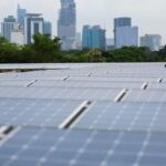 A technician in a green shirt walks among rows of solar panels with the skyline of Jakarta, Indonesia, in the background